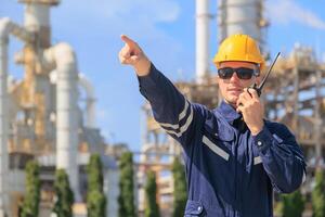Petroleum industry engineer worker working outdoor. Refinery plant oil and gas service team control operate maintenance front of large complex gas pipe building with radio. photo
