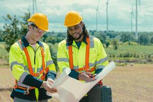Engineer team mix black and white male workers with floor plan at Wind Turbines field working survey at wind electricity generator farm field outdoor. photo