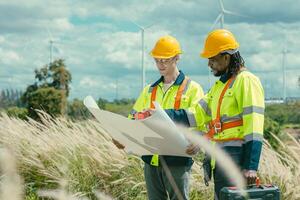 Engineer team mix black and white male workers with floor plan at Wind Turbines field working survey at wind electricity generator farm field outdoor. photo