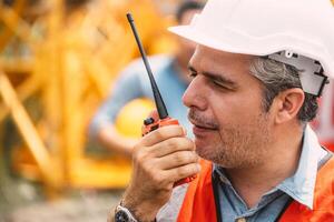 Senior construction engineer worker control operate construction site with radio communication. Foreman order crane tower working by walkie talkie radio. photo