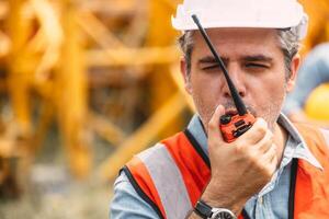 Italian worker engineer construction site control radio operation. Foreman operate crane tower working order by walkie talkie. photo