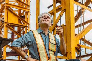 Italian worker engineer construction site control radio operation. Foreman operate crane tower working order by walkie talkie. photo