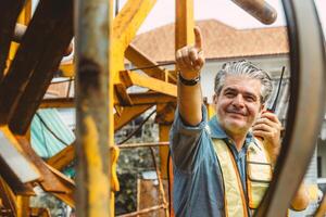 Italian worker engineer construction site control radio operation. Foreman working crane working order by walkie talkie. Happy worker portrait. photo