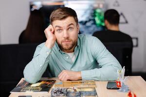 Man with board game piece while practicing strategy in home alone. A man plays a board game with cards and figures, expressing different emotions photo