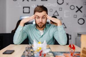 Man with board game piece while practicing strategy in home alone. A man plays a board game with cards and figures, expressing different emotions photo