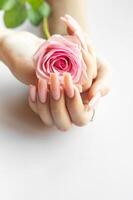 A person with long pink nails gently holding a soft pink rose against a light background photo