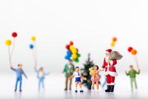 Miniature Santa Claus holding a gift surrounded by children and colorful balloons photo