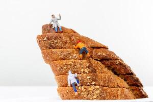 Miniature figurines climbing a stack of multigrain bread slices, resembling a rugged mountain photo
