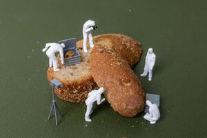 Miniature figurines dressed as forensic investigators examining bread slices with equipment photo