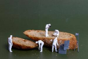 Miniature figurines dressed as forensic investigators examining bread slices with equipment photo