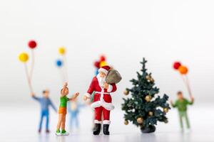 Miniature Santa Claus holding a gift surrounded by children and colorful balloons photo
