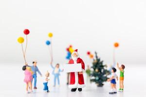 Miniature Santa Claus holding a gift surrounded by children and colorful balloons photo