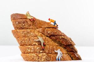 Miniature figurines climbing a stack of multigrain bread slices, resembling a rugged mountain photo