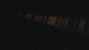 vicino su di il libri su il scaffali di il biblioteca. azione filmato. buio leggero nel un' camera con libri. video