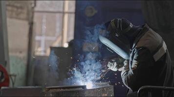 Welder welds metal structures at factory. Stock clip. Masked welder is working on assembly of metal structures. Professional worker with welding at industrial plant video