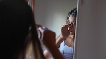 A woman is standing before a mirror, applying her makeup while enjoying the natural light video