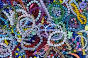 A variety of colorful beaded necklaces and bracelets laid out on a surface. Some beads are round and smooth, while others are irregularly shaped. photo