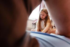 A young girl sits on the floor, looking down thoughtfully, from a low-angle perspective photo