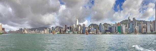 Panoramic daytime view of Hong Kong skyline, surrounded by lush green hills and a busy harbor photo