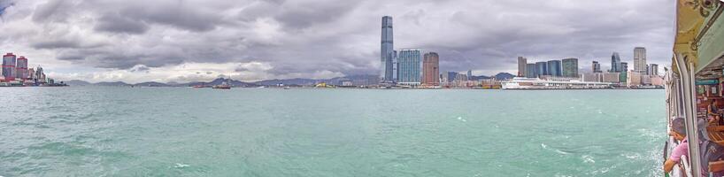 Panoramic daytime view of Hong Kong skyline, surrounded by lush green hills and a busy harbor photo