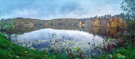 Panoramic view of a serene lake surrounded by a colorful autumn forest with vibrant foliage and reflections photo