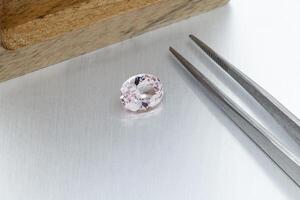 macro mineral faceted stone Morganite with tweezers on a gray background photo