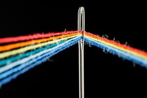 multi-colored threads for sewing in the form of a rainbow pass through an antique needle on a black background photo