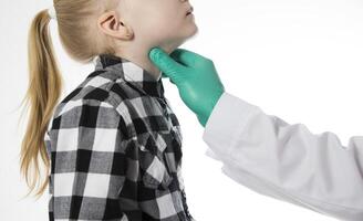The hand of a pediatrician doctor probes the sore throat of a seven-year-old girl who has a sore throat. Inflammation of the lymph nodes, bacterial and viral infection. Copy space for text photo