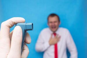 A doctor is holding an asthma inhaler with salbutamol, in the background is a man who is choking on asthma, bronchodilator medications photo