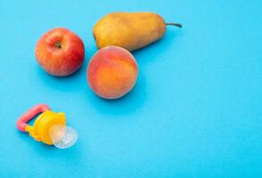 Fruits on a blue background next to a children's nibbler, close-up. Cognitive nutrition with vitamins and the development of the chewing reflex in children, close-up photo