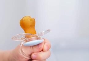 The baby is holding a torn and chewed silicone pacifier in his hands. Concept of teething in children, sucking reflex. Copy space for text photo