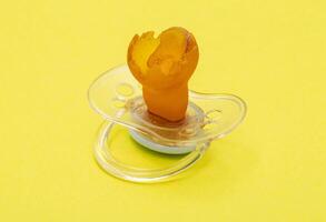 Low-quality torn baby silicone pacifier on a yellow background, close-up. Concept of the anatomical shape of the pacifier, teething in children. photo