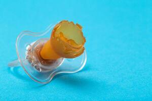Torn and chewed baby silicone pacifier on a blue background, close-up. The concept of teething in children. Copy space for text photo