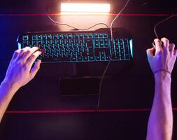 Gamer plays game at computer club, fingers click on buttons of gaming mouse, keyboard with RGB lighting. Professional E-sport tournament, Cyber team. Real-time strategy shooter. Modern equipment photo