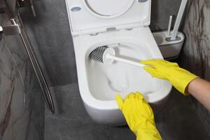 Washing and cleaning the toilet with a brush and detergent to remove dirt, limescale and urinary stone, close-up. Cleaning company services photo