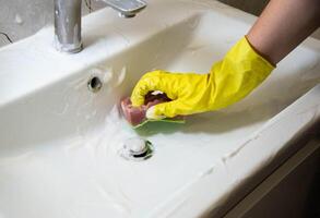 A girl washes and cleans the sink with a cleaning agent wearing yellow rubber gloves. Whitening and shine product, close-up. Copy space for text photo