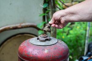 A broken valve of a gas cylinder in a hand against the background of a red gas cylinder. Propane gas leak and explosion concept. Copy space for text, industry. Safety precautions photo