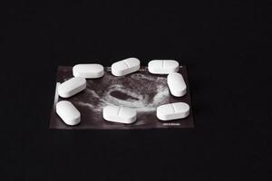 Pregnancy, a shot of uzi and pills on a black background. Abortion, close-up photo