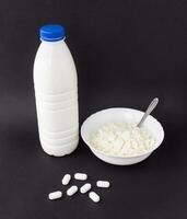 A bottle of milk and a plate of cottage cheese on a black background near lie pills of antibiotics, close-up, pills photo
