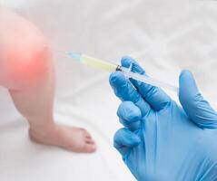 A doctor in medical gloves holds a syringe with plasma to inject a plasma into a patient with a knee that has inflammation, close-up, plasma-lifting photo