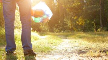 A man with a package of garbage in his hands with plastic in the forest against the backdrop of a forest road, a sunset, copy space photo