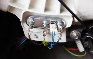An electric heating element with a thermostat is connected with electrical chips. Repair and replacement of temperature sensor and heating element, hard water, close-up photo
