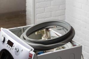 An old, torn, defective rubber hatch seal is standing near the washing machine. Spare parts replacement, industry, close-up. Copy space for text photo