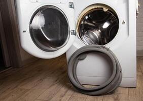 An old, torn, defective rubber hatch seal is standing near the washing machine. Spare parts replacement, industry. Copy space for text photo