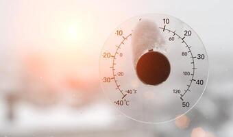 The rays of the setting sun in the sky against the background of a street thermometer with a snow cap on the window. Snowy weather and warming concept. Weather forecast Copy space for text photo