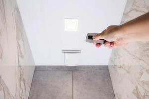 A man holds in his hand an exhaust ventilation control panel and a light control in the bathroom. Copy space for text photo