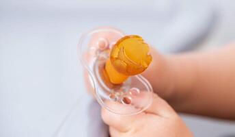 The baby is holding a torn and chewed silicone pacifier in his hands. Concept of teething in children, sucking reflex. Copy space for text photo