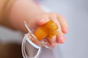 A baby's pacifier is chewed and torn in a baby's hand, close-up. Concept of teething in children, problems with bite. Copy space for text photo