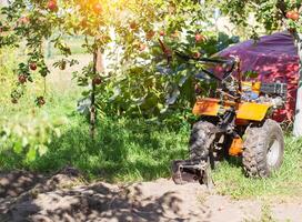 A multifunctional walk-behind tractor stands under an apple tree in summer in sunny weather, industry. Technique for assistance in agriculture. Copy space for text photo