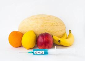 Fruits on a white background bananas, orange, melon, lemon and nectarine, next is a syringe with gmo and nitrates, genetically modified organism, fruit photo